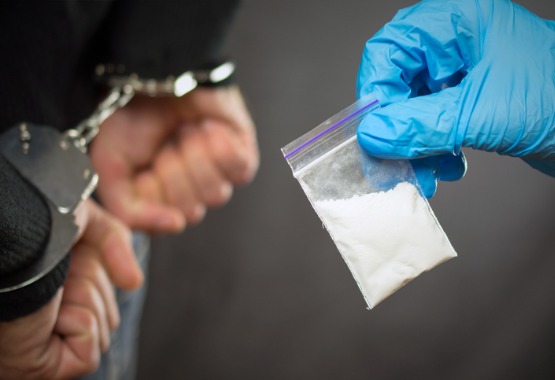 Person holding up small bag of drugs as someone else is being handcuffed and arrested for drug crimes in Peoria IL