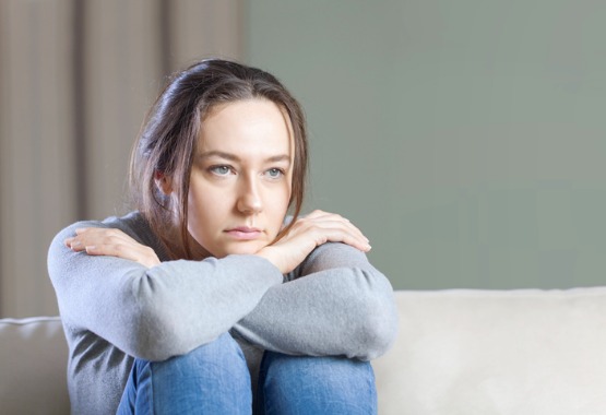 A depressed woman sits with her arms wrapped around herself before consulting a Domestic Abuse Attorney in Peoria IL