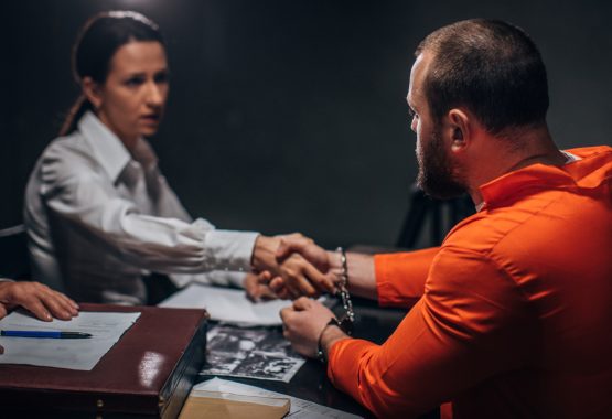 A man in a prison jumpsuit shaking hands with an attorney helping with their criminal defense in Central Illinois